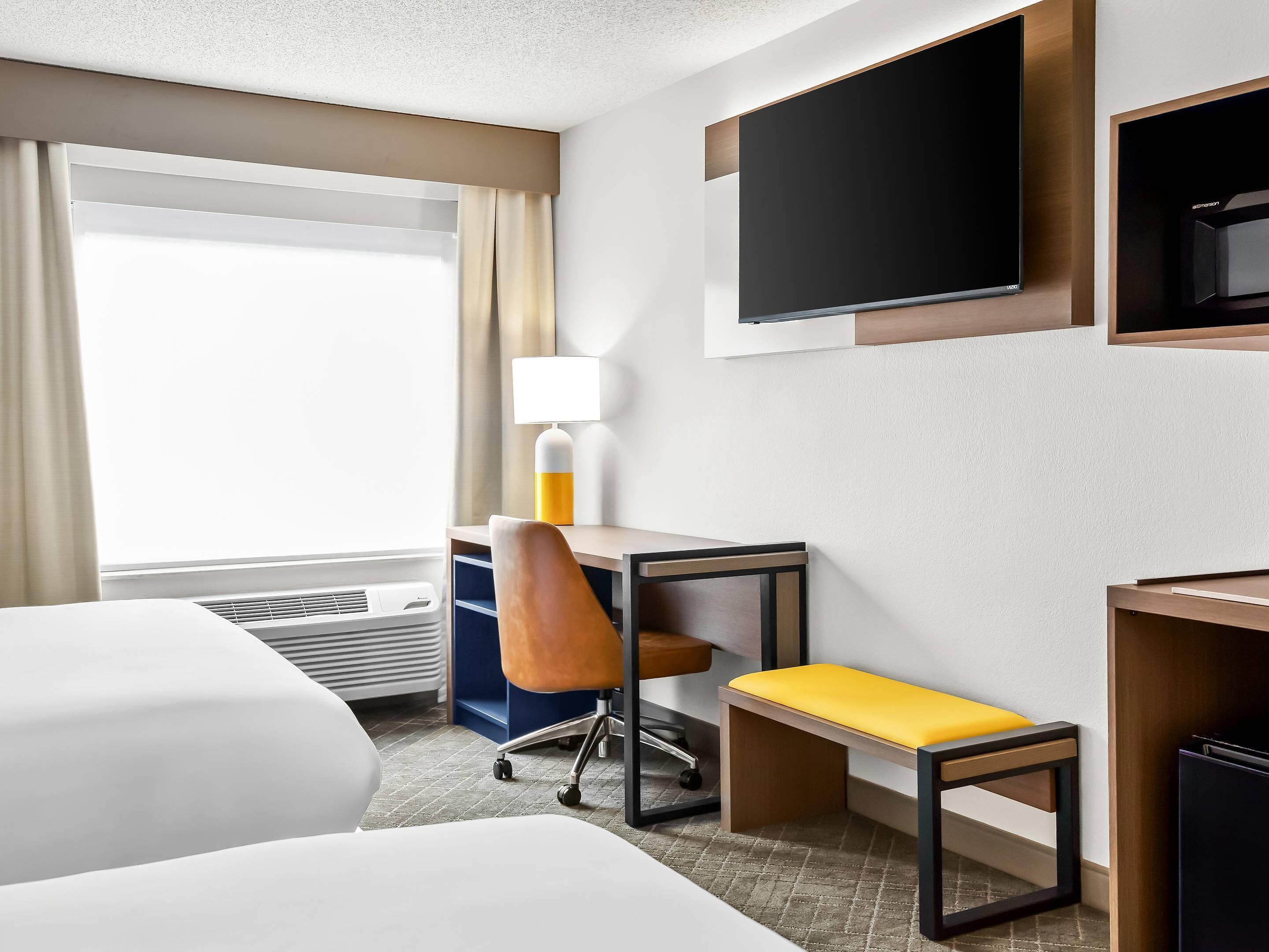 Een hotelkamer met een bed, een bureau met stoel, een televisie en een raam met gordijnen.