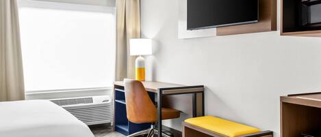 A hotel room with a bed, a desk with a chair, a TV, and a window with curtains.