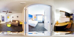 A modern hotel room with a bed, a sofa, a desk, and a ceiling fan.