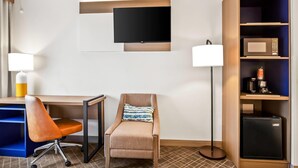 Ein Hotelzimmer mit Schreibtisch, Stuhl, Fernseher, Lampe und Minibar.