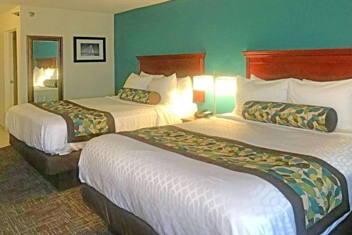 A hotel room with two beds, a mirror, a framed picture, and a nightstand with a lamp.