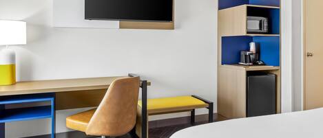 Una habitación de hotel con cama, escritorio con silla, televisor, cafetera y microondas.
