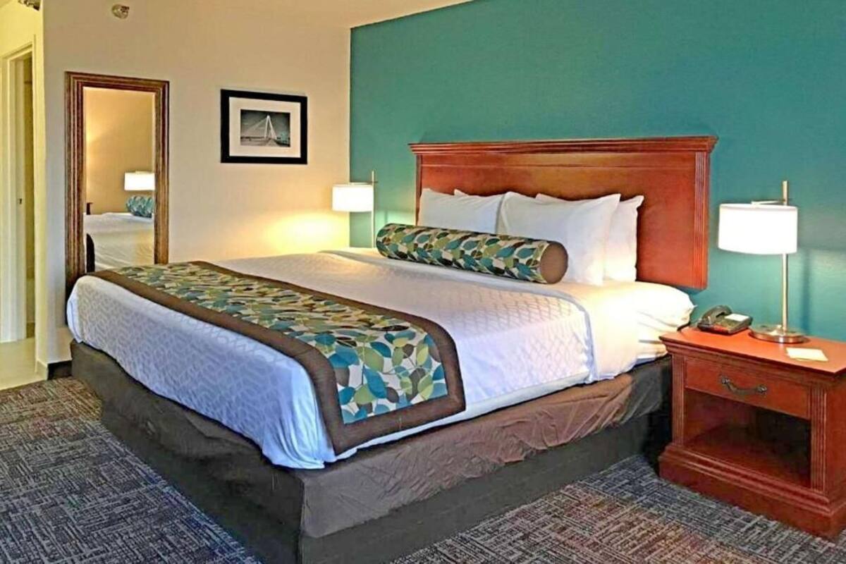 A hotel room with a bed, bedside lamps, a nightstand, and a mirror.