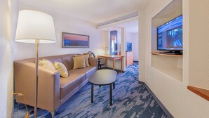 Habitación de hotel con sofá, una mesita, escritorio, lámpara y televisión.