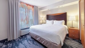 Habitación de hotel con una cama grande, una mesita de noche con lámpara, una ventana con cortinas y vista a la ciudad.