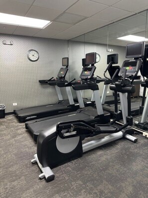 Une salle de sport équipée de tapis de course, de vélos d’appartement et d’un banc de musculation.