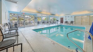 Una piscina interior con paredes de vidrio transparente, una zona de estar junto a la piscina e iluminación empotrada en el techo.