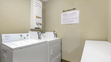 Une salle de bain d’hôtel équipée d’un lave-linge et d’un sèche-linge Whirlpool, d’un lavabo et de toilettes. Un panneau indique que la buanderie est réservée aux clients de l’hôtel.