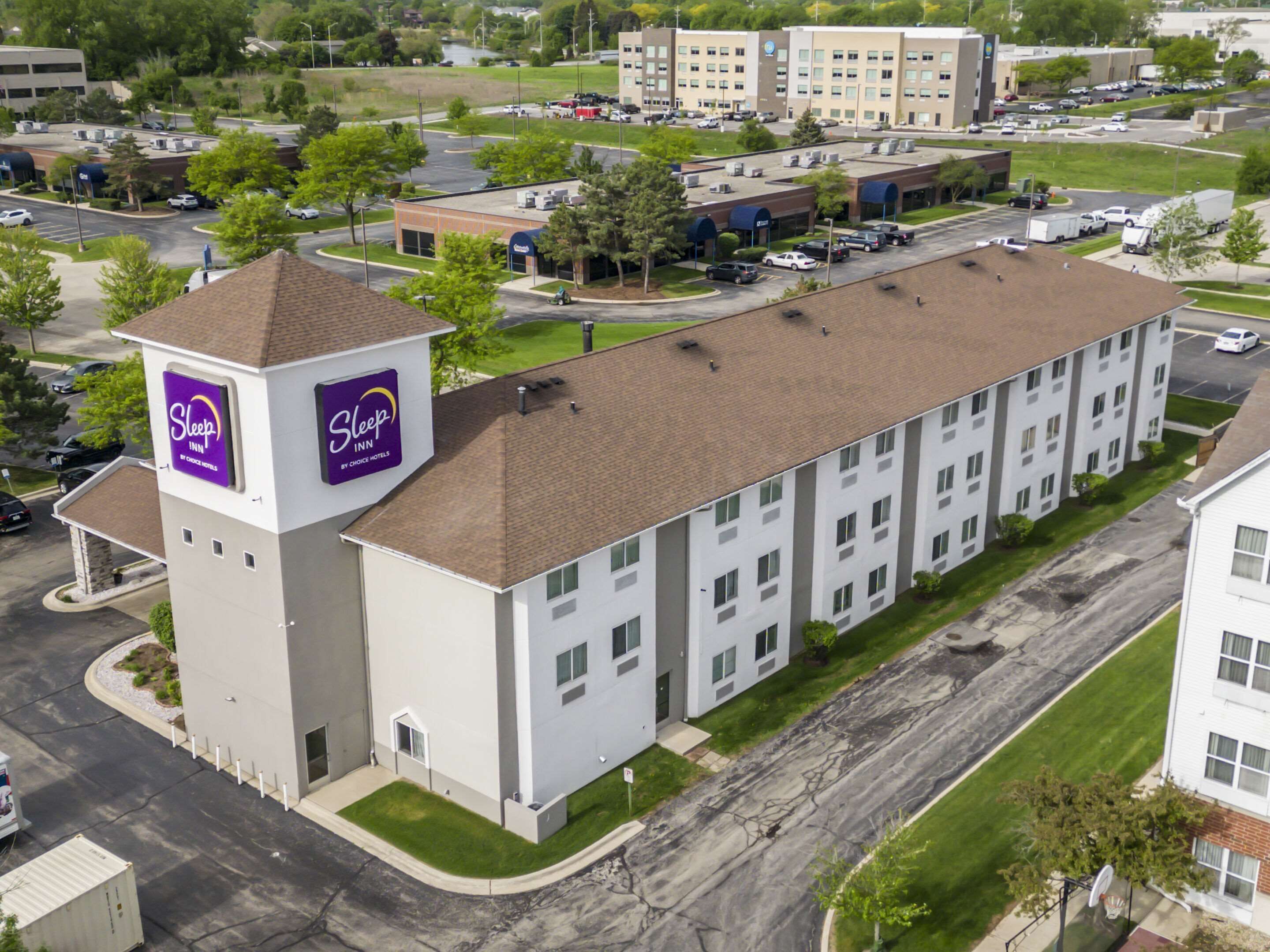 A Sleep Inn by Choice Hotels building with a central tower, parking lot, and surrounding greenery.