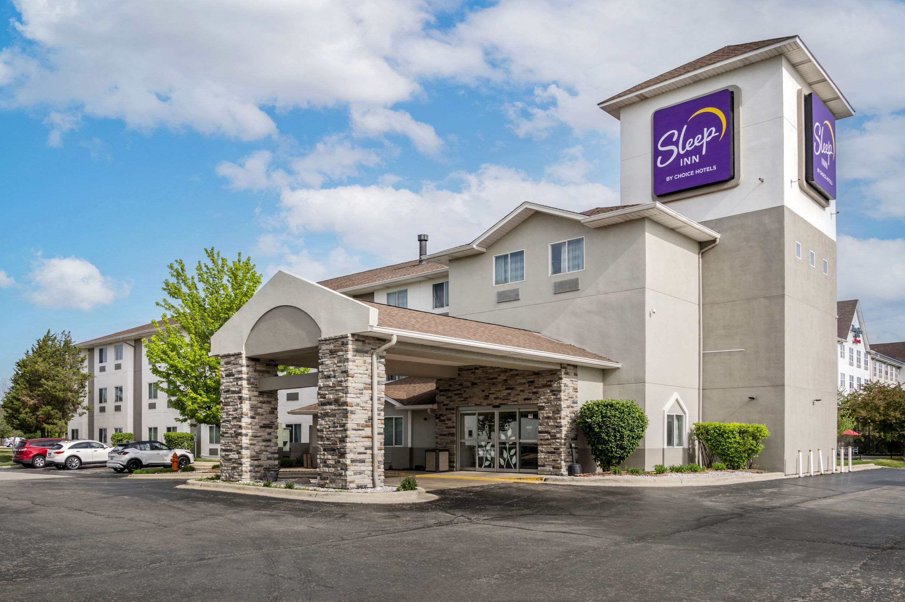Edificio de Sleep Inn afiliado a Choice Hotels, con fachada de piedra, entrada cubierta y estacionamiento con automóviles.