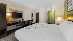 Una habitación de hotel con una cama grande, un escritorio con una computadora, un televisor y una puerta que da a otra habitación.