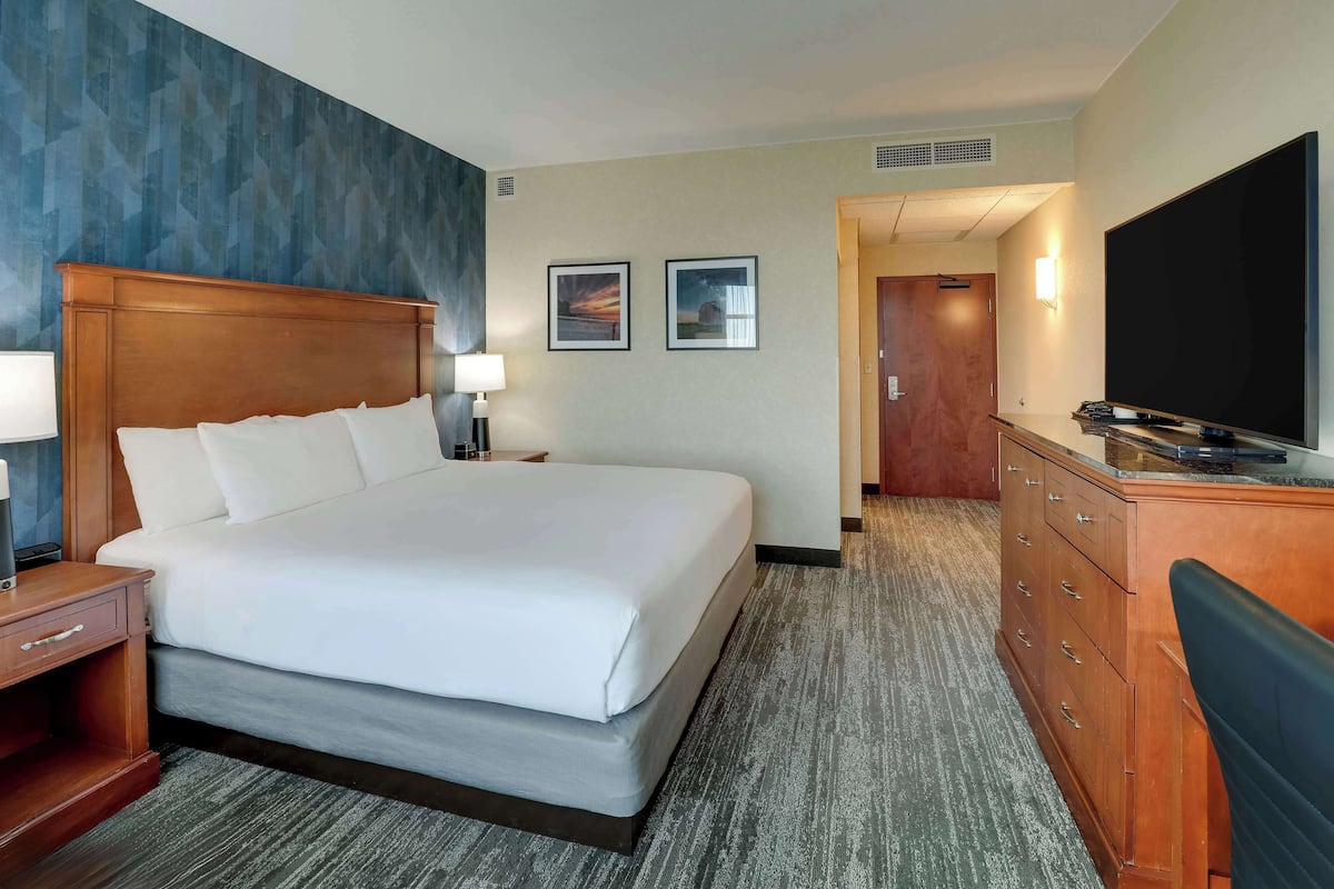 A hotel room with a large bed, a wooden nightstand, a dresser, a flat-screen TV, and two framed pictures on the wall.