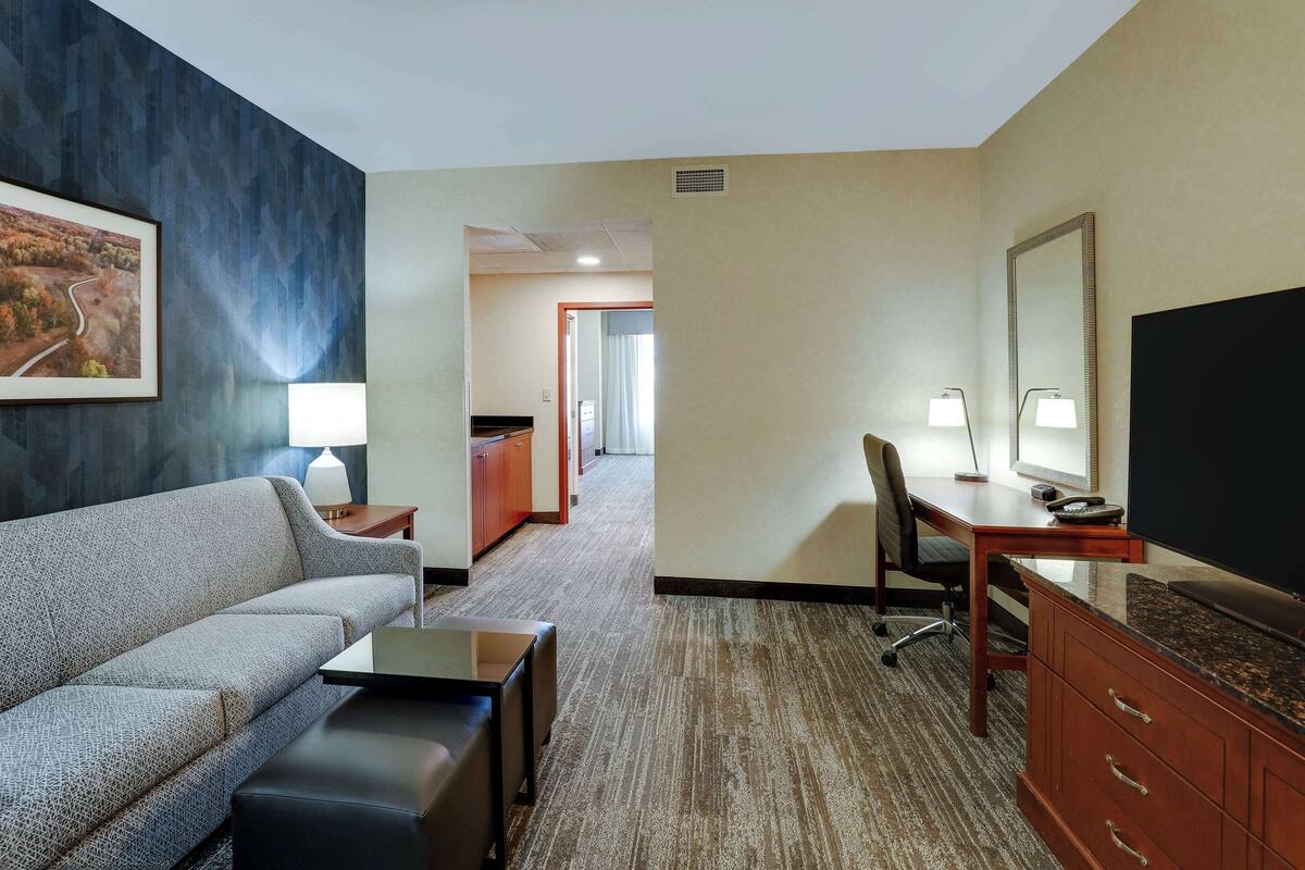 A hotel room with a sofa, a desk, a television, and a mirror.