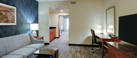 A hotel room with a sofa, a desk, a television, and a mirror.