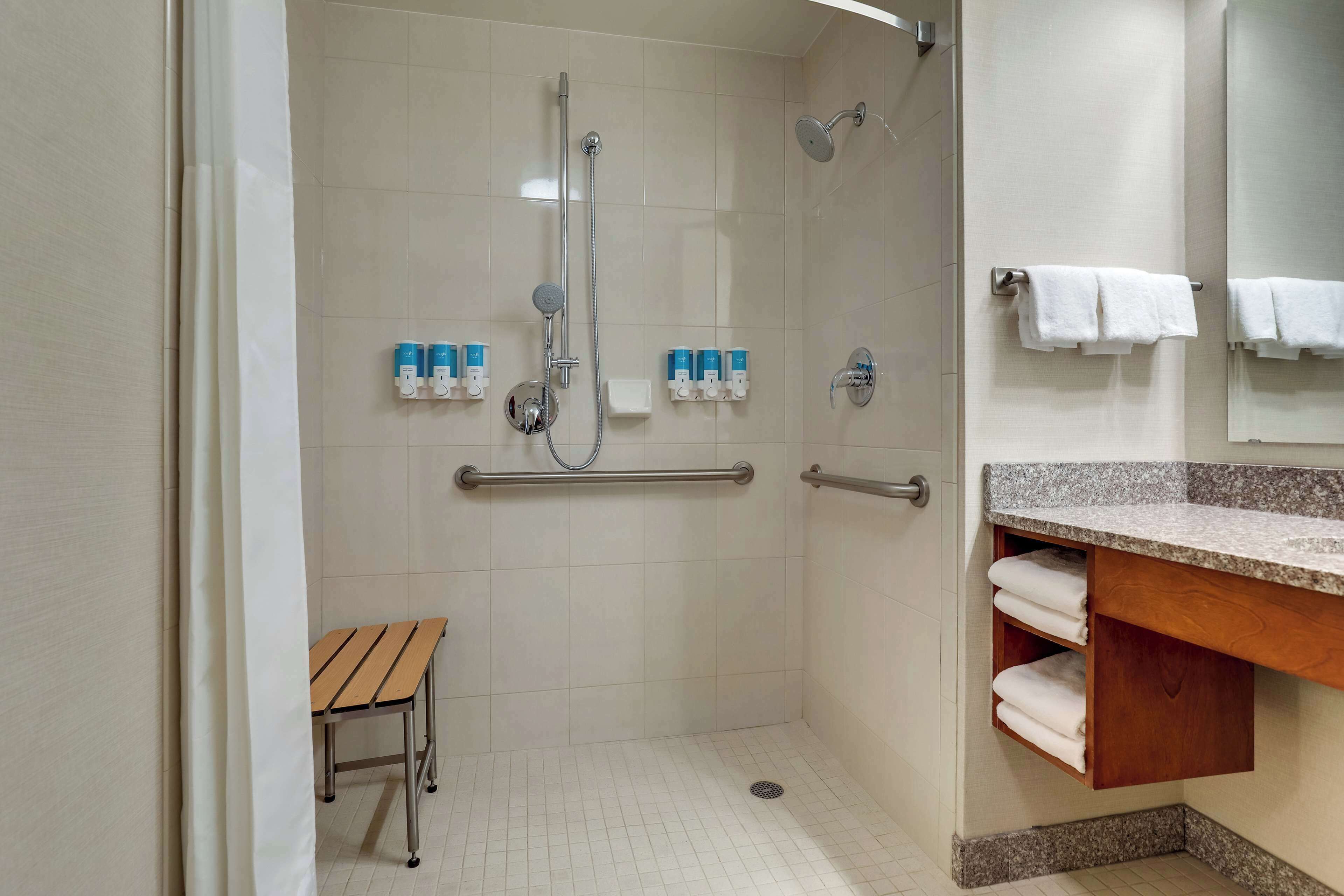Ducha con barandilla, banco y lavabo con barra para toallas.
