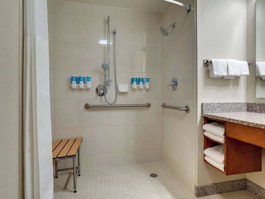 Ducha con barandilla, banco y lavabo con barra para toallas.
