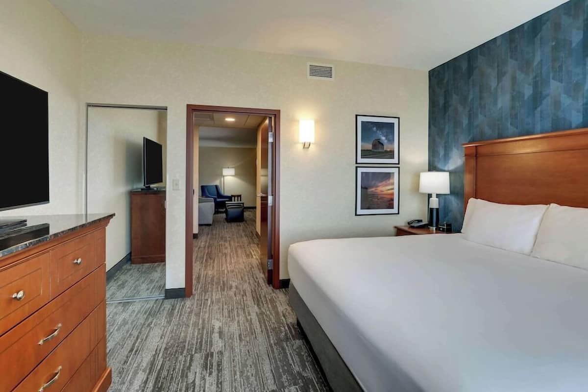 A hotel room with a large bed, a TV, a desk, a chair, and a door leading to a bathroom.