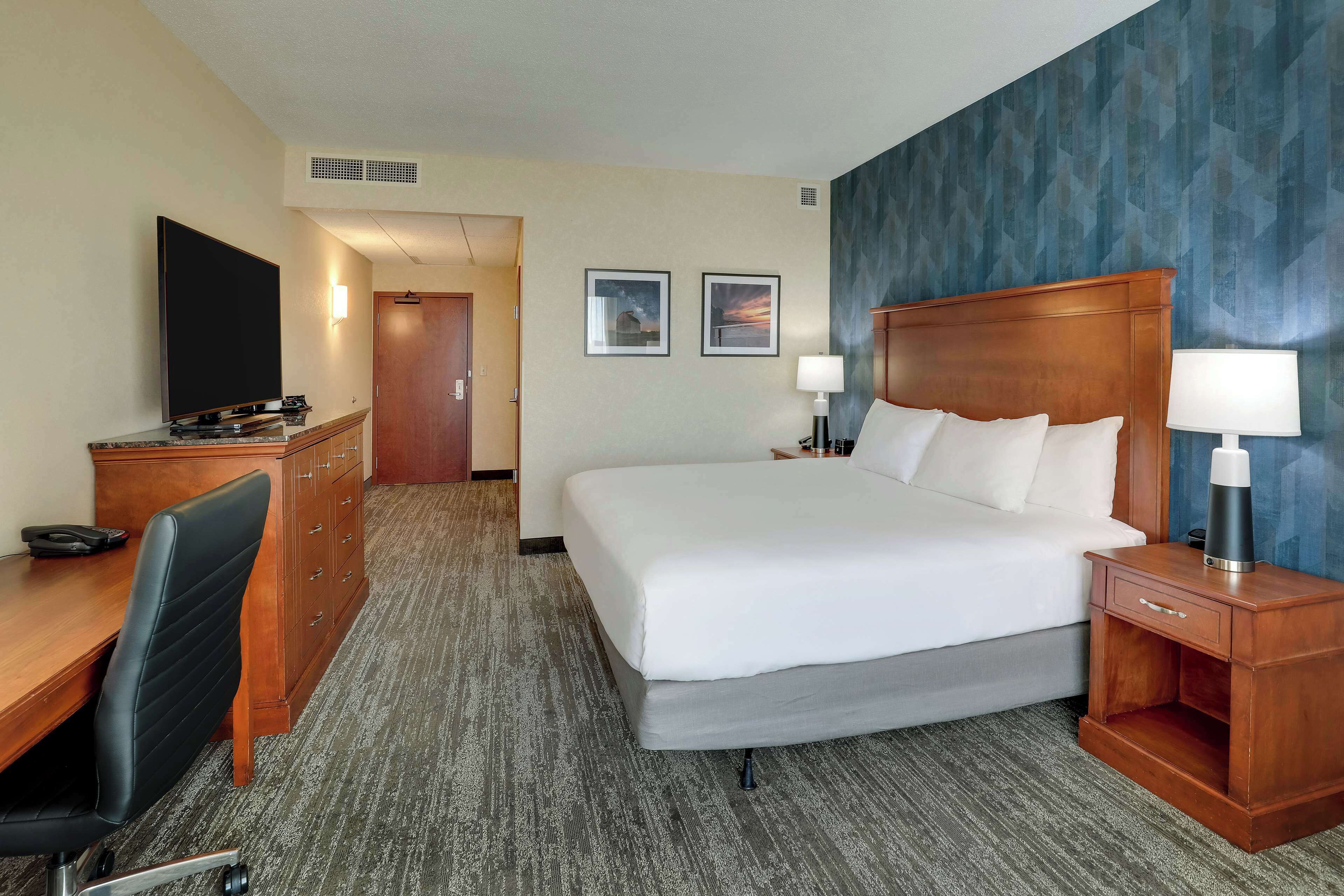 A hotel room with a large bed, a desk with a chair, a television, and two framed pictures on the wall.