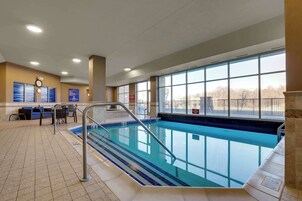 Una piscina interior con paredes de vidrio transparente, un reloj y una zona de recepción con sillas azules.