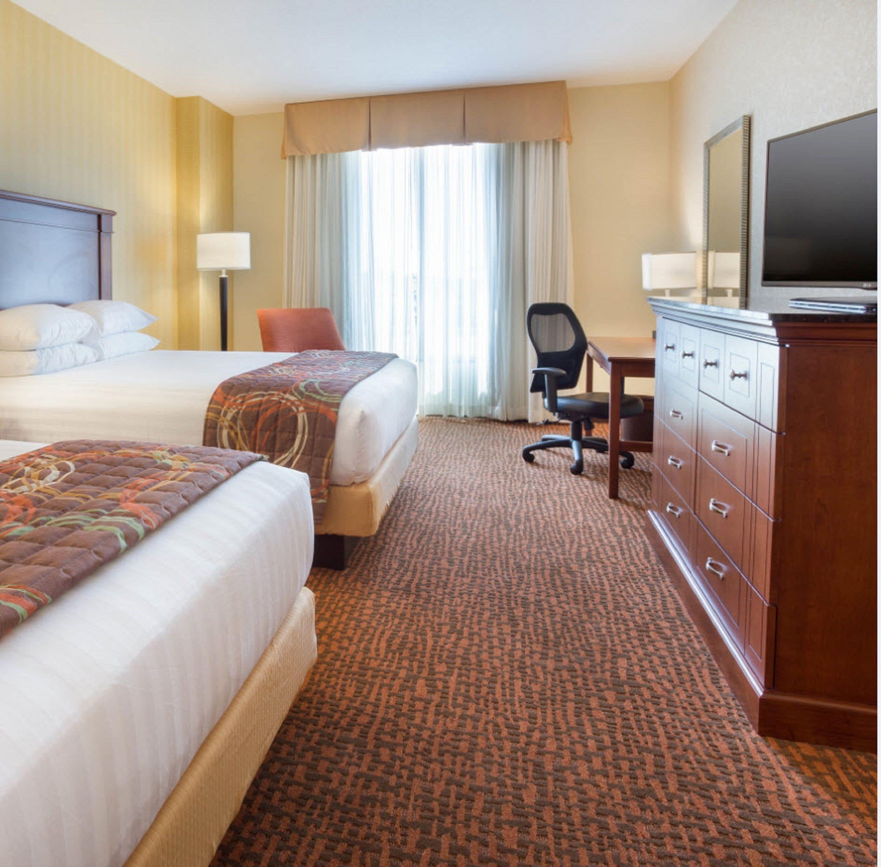 A hotel room with two beds, a desk, a chair, a television, and a dresser.