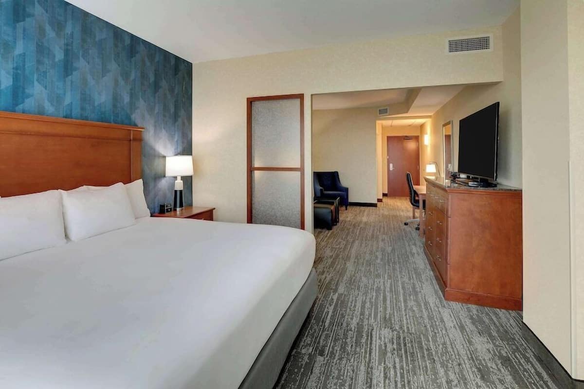 A hotel room with a large bed, a desk with a flat-screen TV, a chair, and a wardrobe.