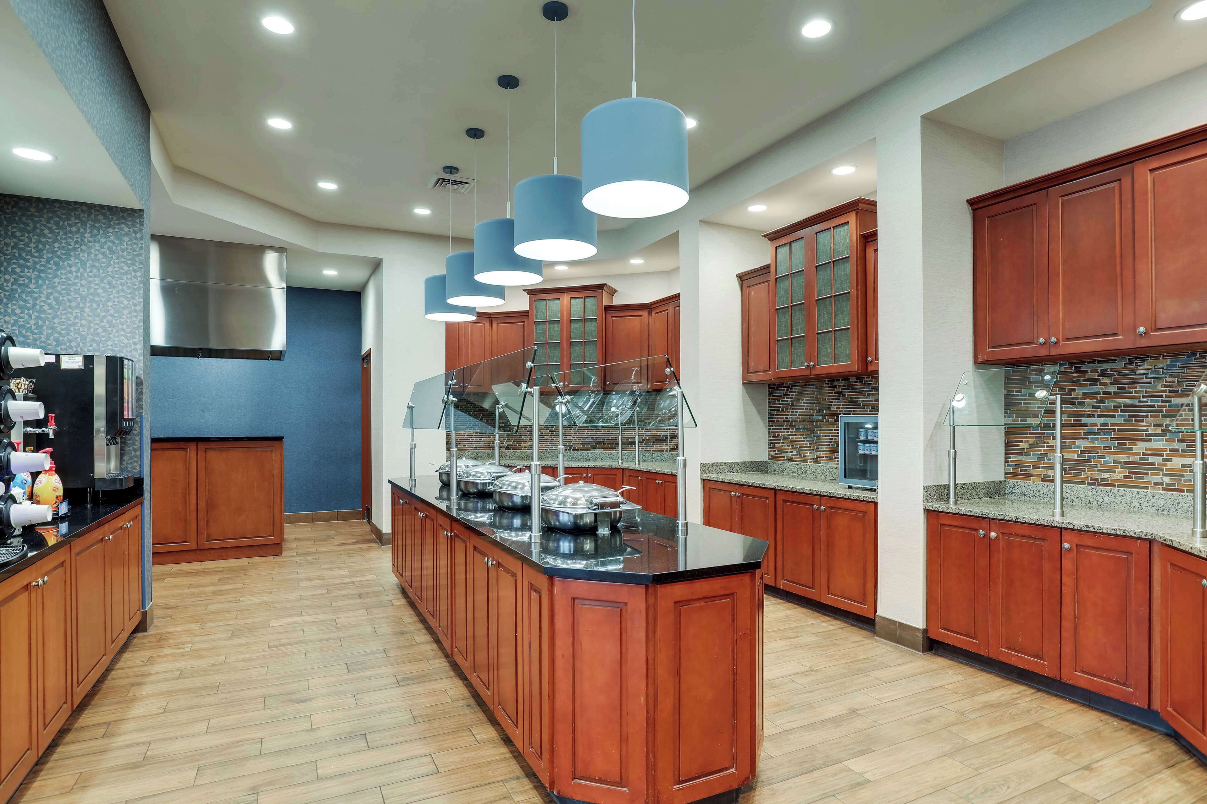 A modern kitchen with wooden cabinets, a central island, and pendant lighting.