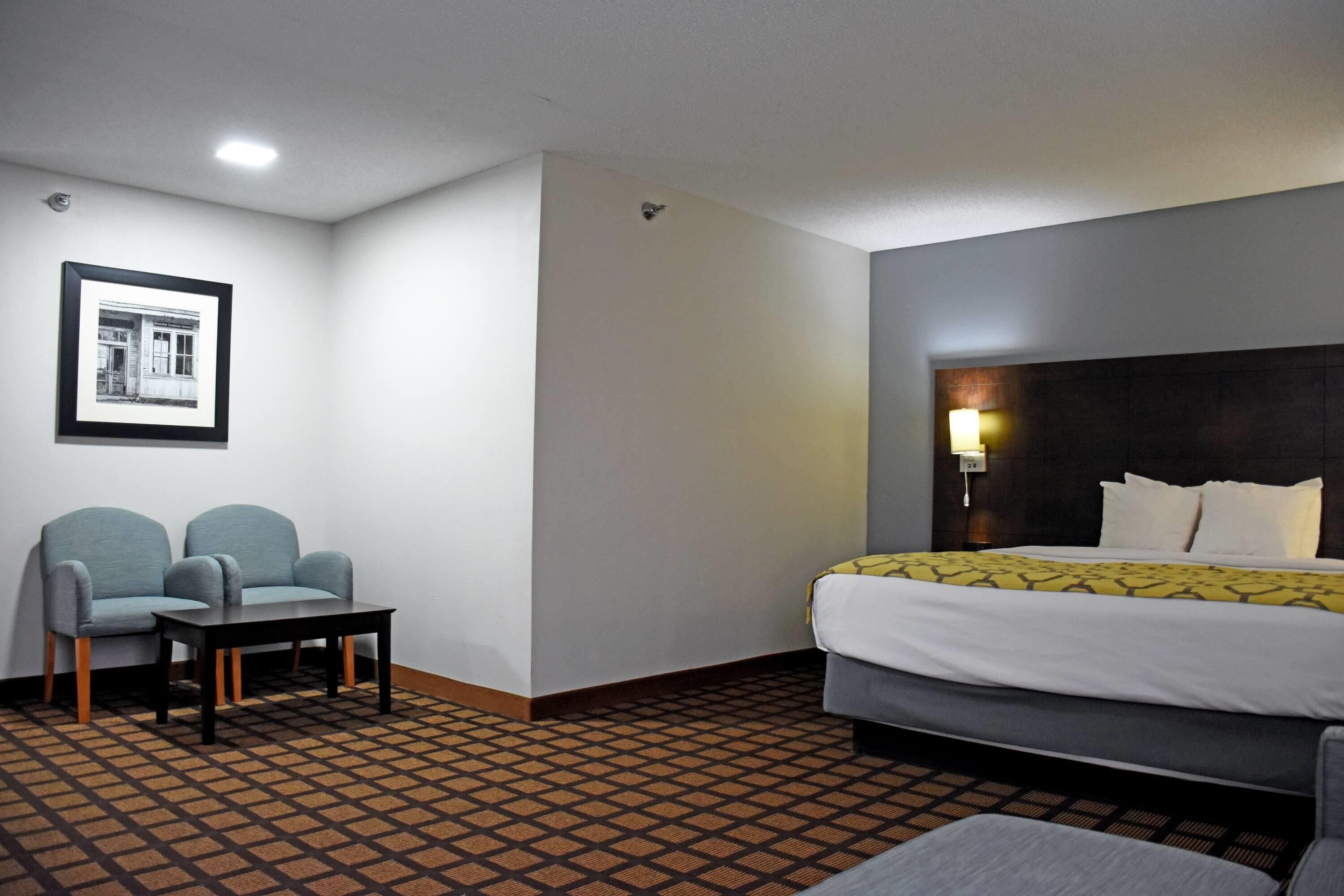 Habitación de hotel con cama, dos sillones, una mesita y un cuadro en la pared.