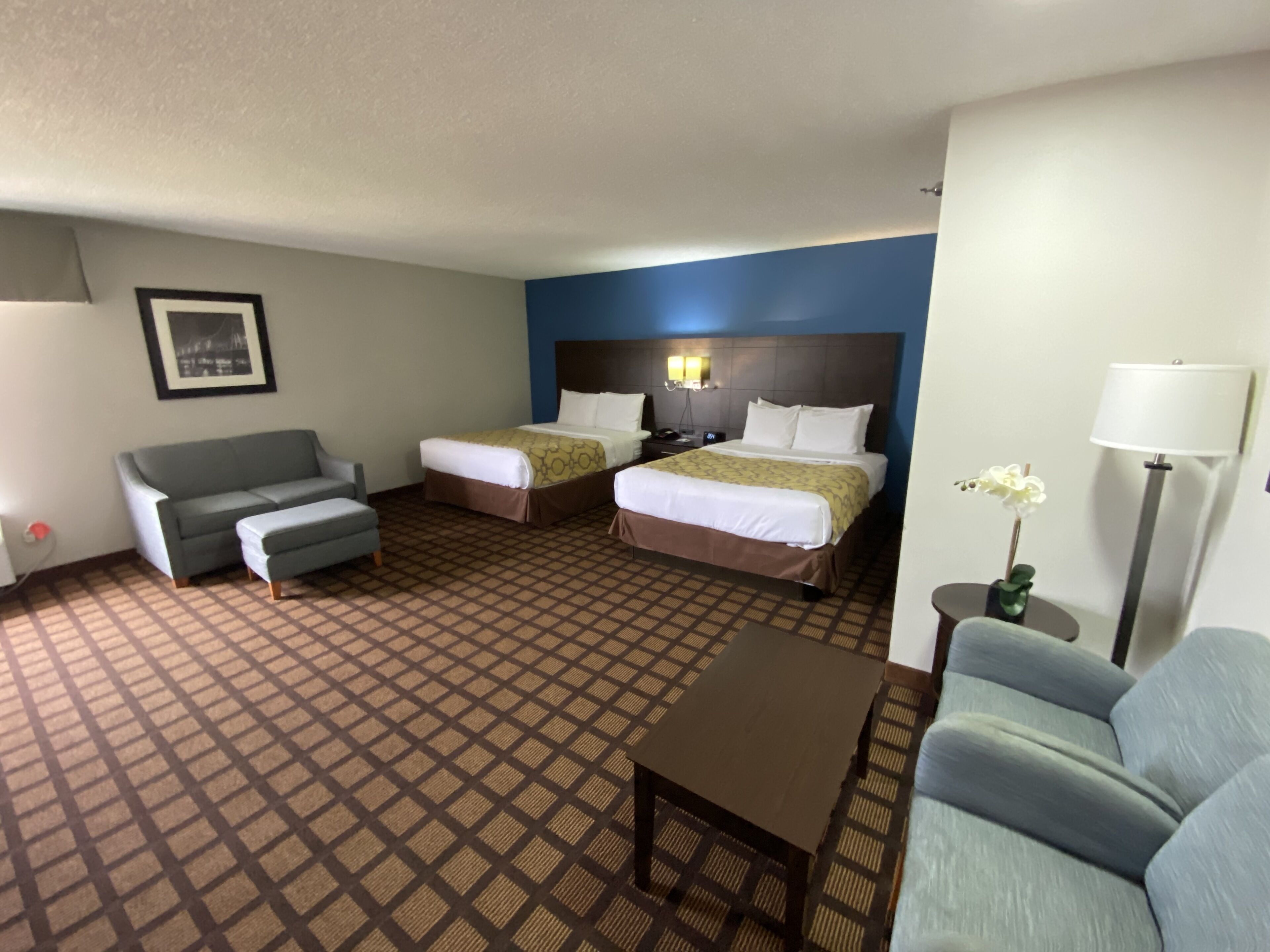 A hotel room with two beds, a sofa, a small table, and a lamp.