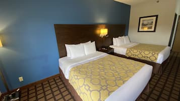 A hotel room with two beds, a headboard, a nightstand, a lamp, and a framed picture on the wall.