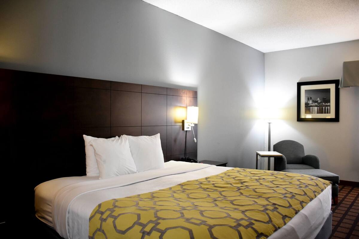 Een hotelkamer met een groot bed, een nachtkastje, een stoel, een lamp en een lijst met een afbeelding aan de muur.