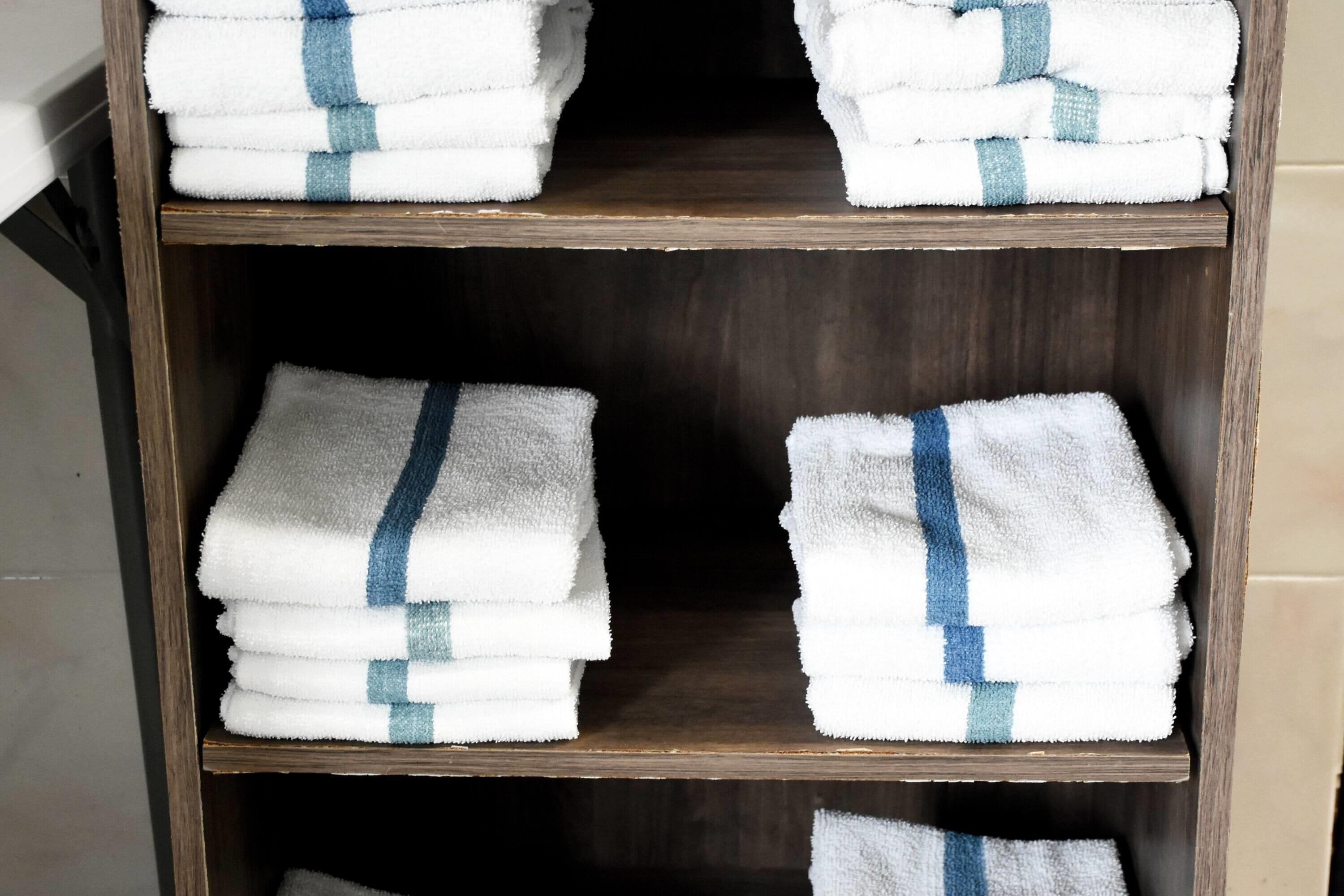 A wooden shelf with four stacks of white towels with blue stripes.