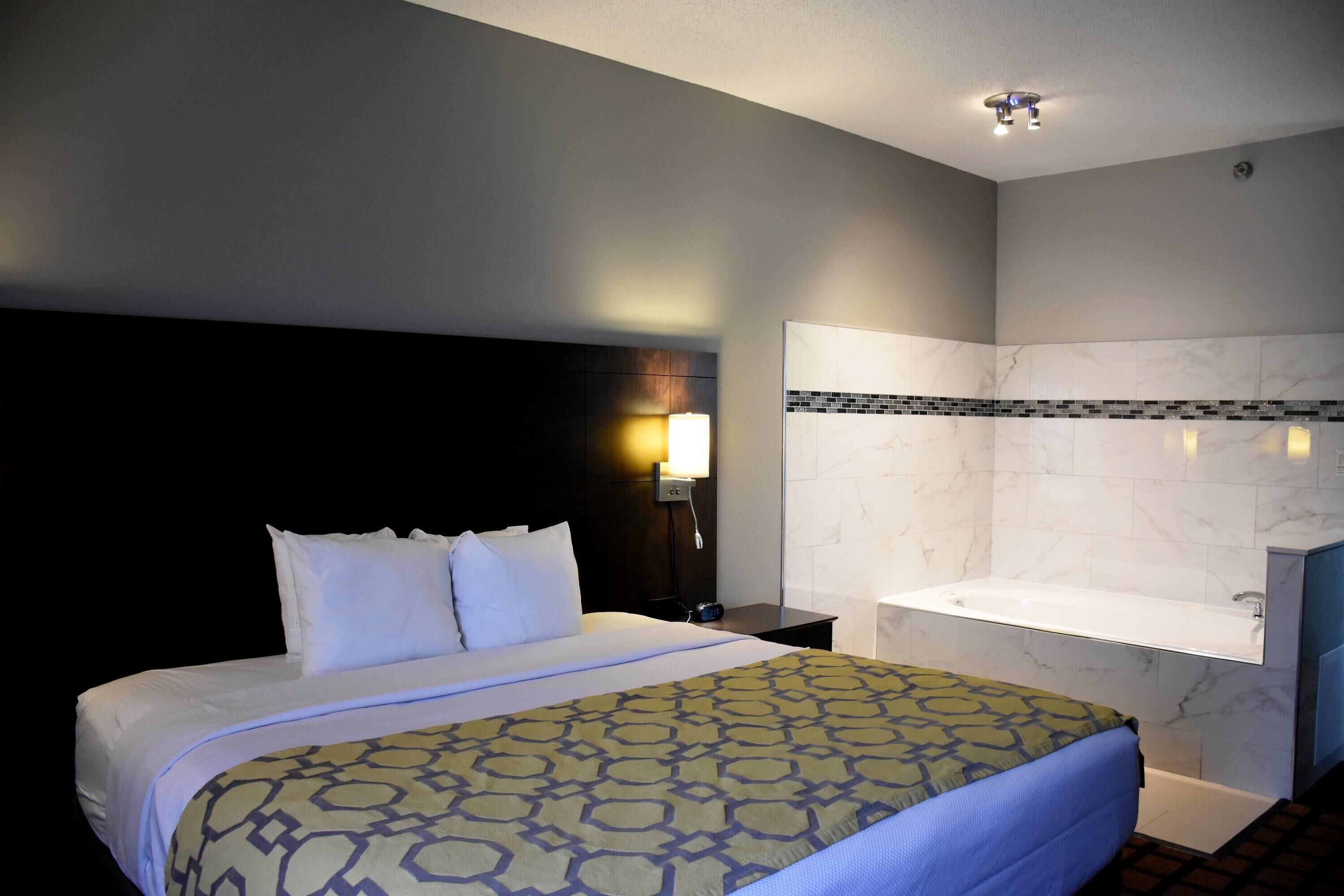 Ein Hotelzimmer mit einem großen Bett, einem Nachttisch mit Lampe, einem Badezimmer mit Badewanne und einer Marmorwand.