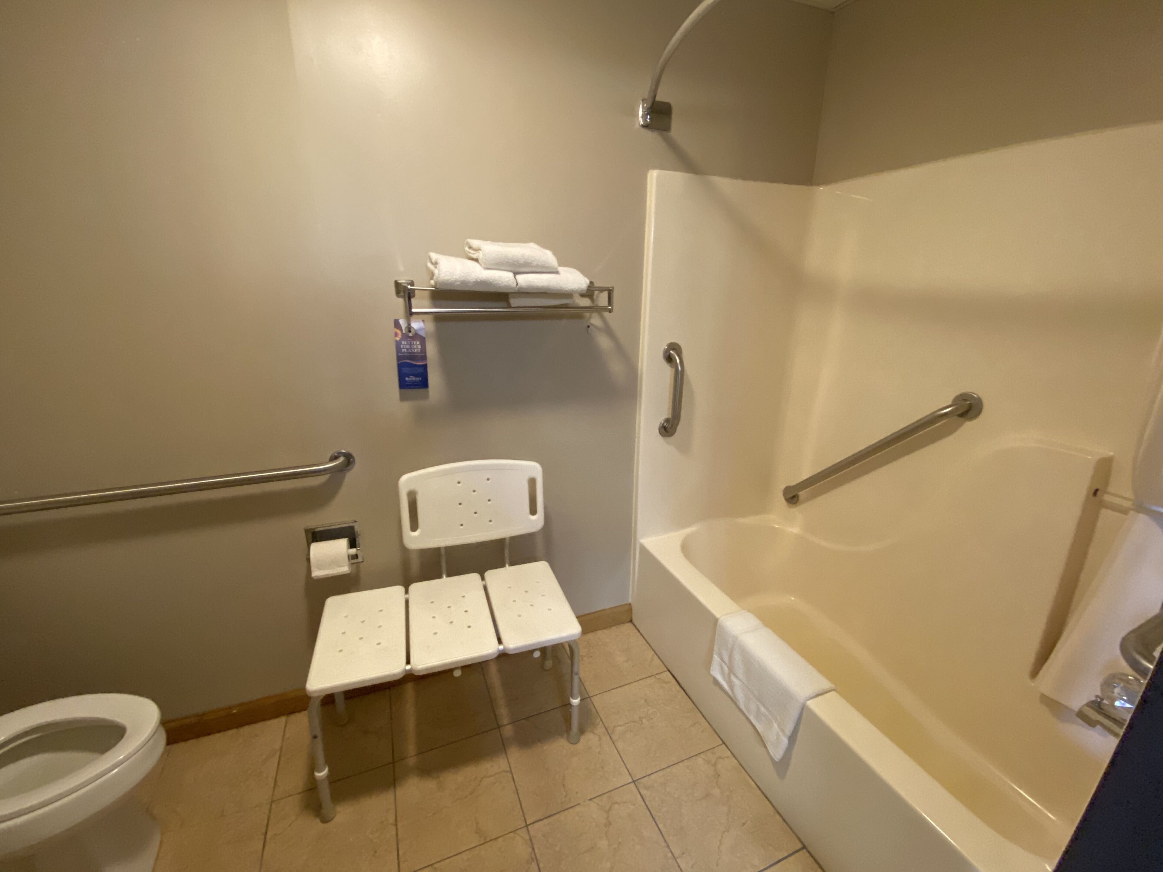 A bathroom with a white toilet, a shower with a grab bar, a white bench, and a towel rack.