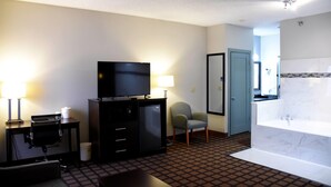 A hotel room with a television, desk, chair, lamp, and a bathroom with a bathtub and mirror. - Baymont by Wyndham Morton (Morton)