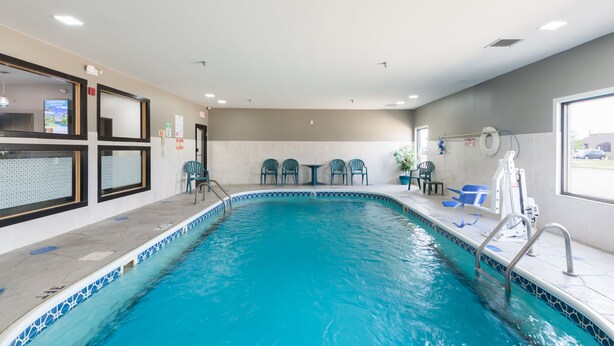 An indoor swimming pool with clear water, surrounded by a tiled deck. There are lounge chairs and a small table in the background. - Baymont by Wyndham Morton (Morton)