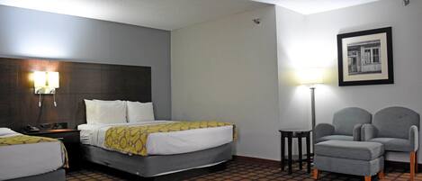 Ein Hotelzimmer mit zwei Betten, einem Schreibtisch, einem Sessel, einer Lampe und einem gerahmten Bild an der Wand.
