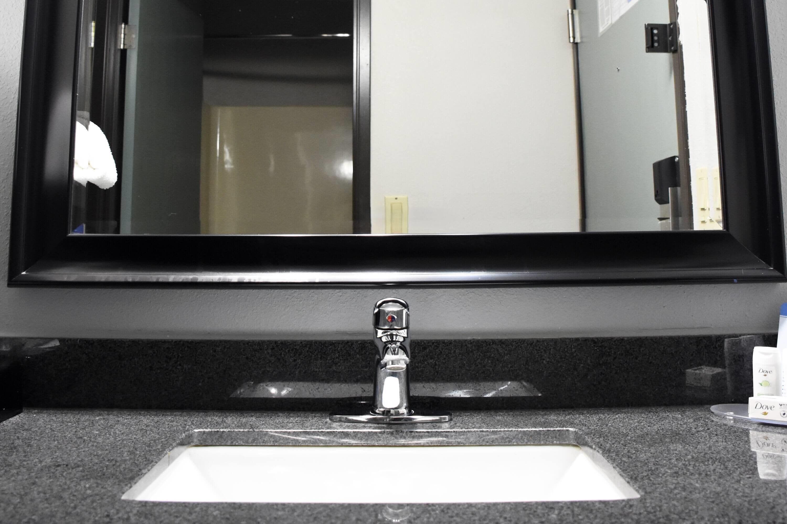 Un lavabo con un espejo encima, una toalla colgada en la pared y artículos de aseo sobre la encimera.