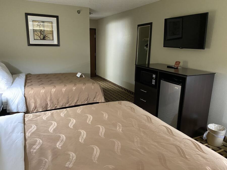 Una habitación de hotel con dos camas, un aparador, un espejo y un televisor.