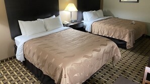 Ein Hotelzimmer mit zwei Betten, einem Nachttisch mit Lampe, einem Telefon und einem gerahmten Bild an der Wand.