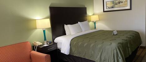 A hotel room with a bed, two bedside lamps, a telephone, a chair, and a framed picture on the wall.