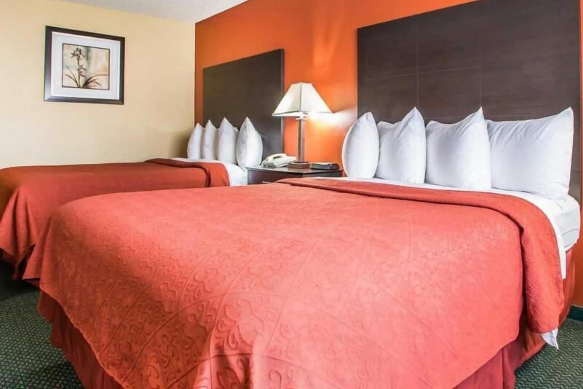 Habitación de hotel con dos camas, una mesita de noche, una lámpara y un cuadro en la pared.