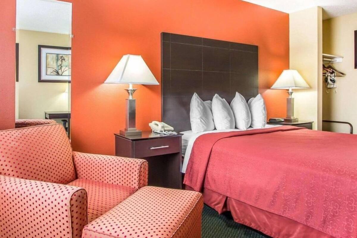 Una habitación de hotel con una cama, dos mesitas de noche con lámparas, una silla, un escritorio y un espejo.