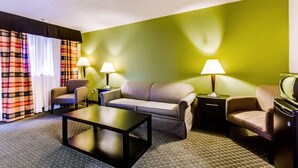 Une chambre d’hôtel avec un mur d’accent vert, un canapé, deux fauteuils, une table basse et deux lampes.