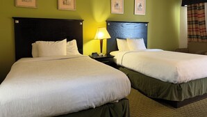 Une chambre d’hôtel avec deux lits, une table de chevet avec une lampe et trois tableaux encadrés au mur.
