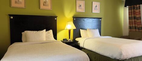 A hotel room with two beds, a nightstand with a lamp, and three framed pictures on the wall.