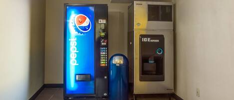 Uma área com máquinas de venda automática, incluindo um dispensador de Pepsi e um de gelo.