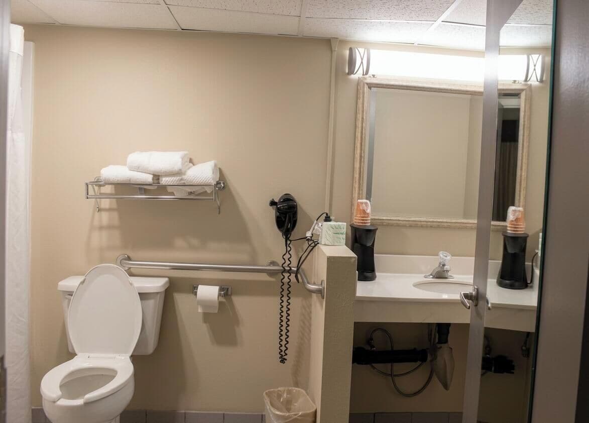Une salle de bain équipée de toilettes, d’un sèche-mains, d’un porte-serviettes, d’un lavabo et d’un miroir.