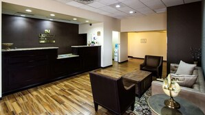 Un espace d’accueil doté d’un comptoir de réception en bois foncé, un espace d’attente avec un canapé et des fauteuils, et un comptoir de réception sur lequel est affiché un panneau indiquant « Quality Inn & Suites by Choice Hotels ».
