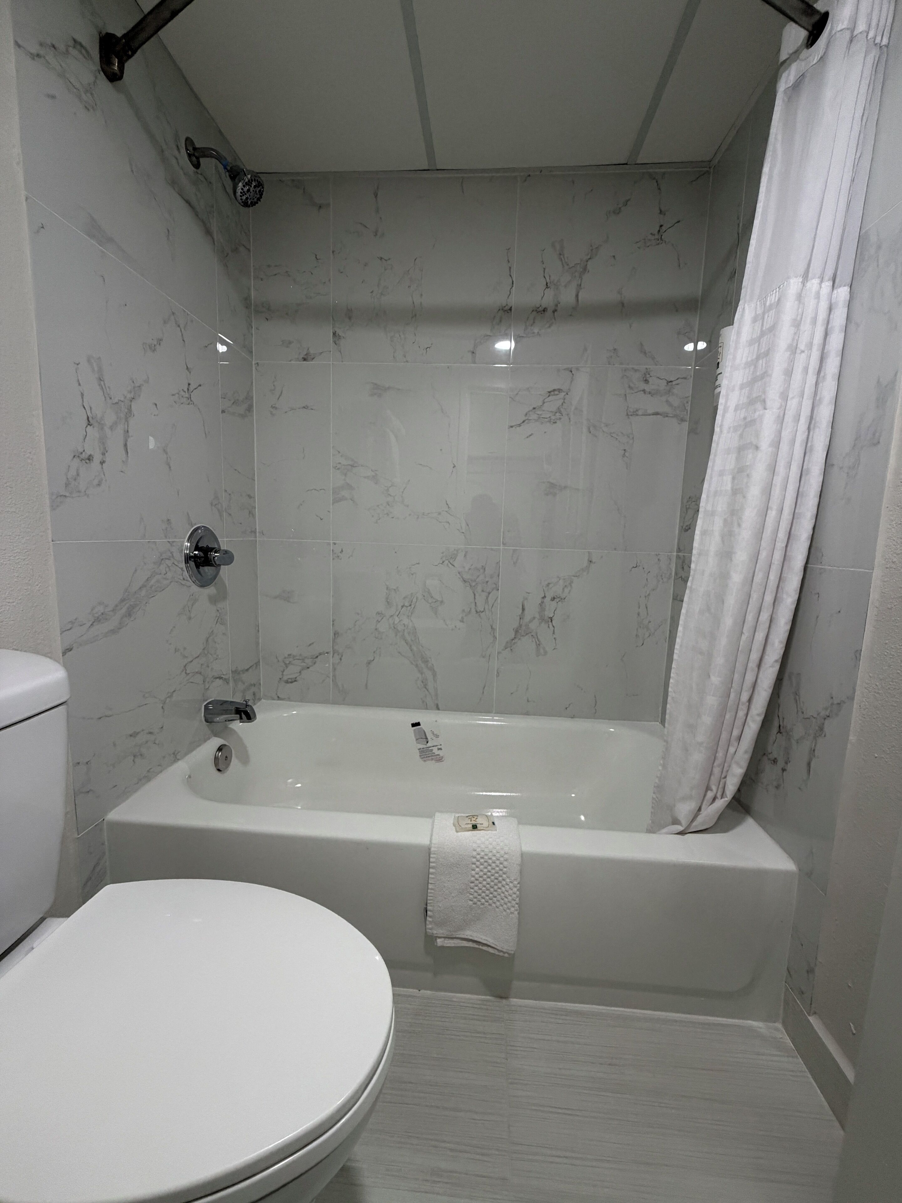 Une salle de bain avec des toilettes blanches, une baignoire équipée d’un pommeau de douche et une serviette accrochée au mur.