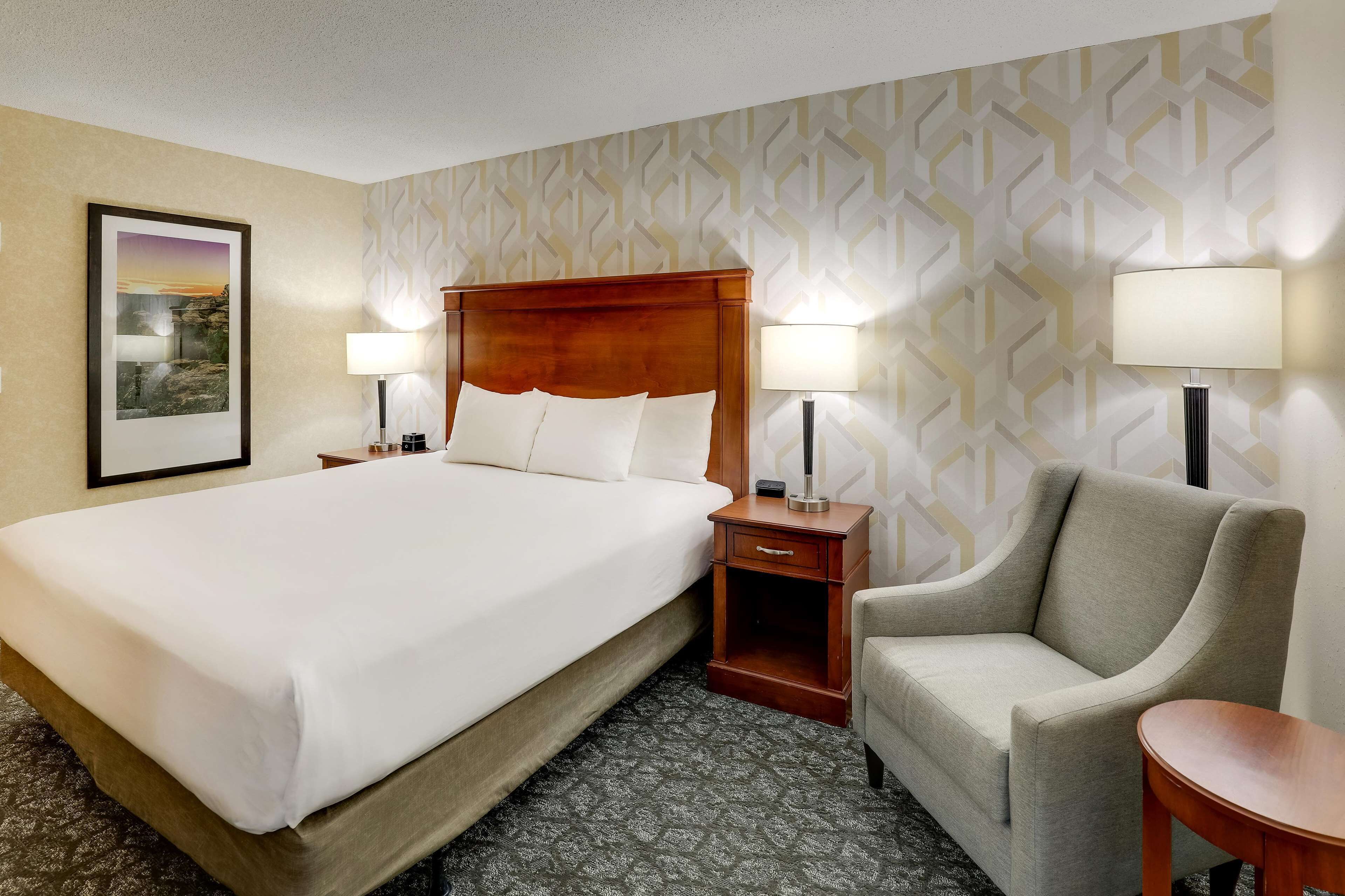 A hotel room with a large bed, two bedside tables with lamps, a chair, and a small table.
